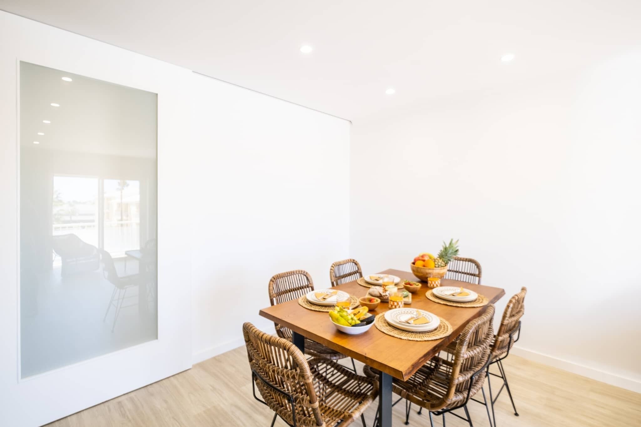 Un coin repas avec une table en bois, dressée pour quatre personnes, entourée de chaises en osier.