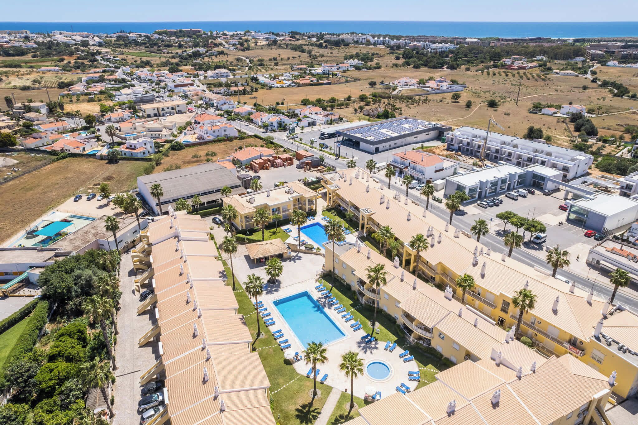 Vista aérea de un complejo turístico con varias edificaciones, una piscina y un estacionamiento.