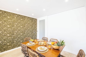 A dining area with a wooden table set for a meal, surrounded by wicker chairs.