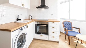 Een kleine keuken met een wasmachine, oven en een stoel.
