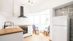 Een moderne keuken met witte kasten, een houten aanrecht, een inbouwoven en een zwarte afzuigkap. Twee blauwe fauteuils staan rond een klein wit tafeltje.