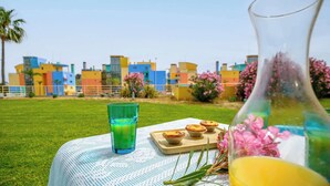 A table with a green drink, a glass of orange juice, and three pastries on a white tablecloth with a cityscape in the background.