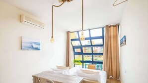 A bedroom with a wooden desk, a bed, a window with curtains, and an air conditioning unit.