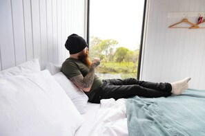 Uma pessoa deitada em uma cama com vista para a janela, um travesseiro branco e um cobertor verde.