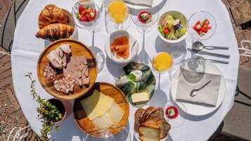 Ein reichhaltiges Frühstücksbuffet auf einem runden Tisch mit Croissants, Käse, Schinken und verschiedenen Früchten sowie Säften.