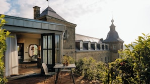 Une maison moderne dotée d’un patio comprenant une table et des chaises, offrant une vue sur un bâtiment traditionnel en arrière-plan, et un chemin de briques menant à l’entrée.