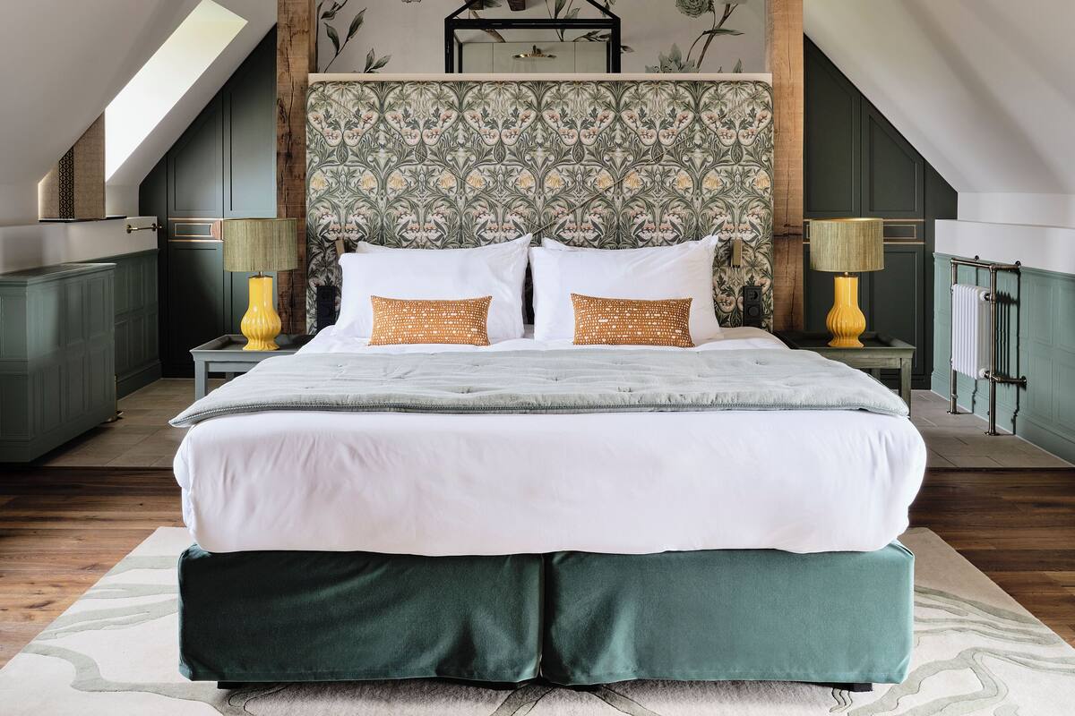 A bedroom with a large bed, two bedside lamps, a radiator, and a wall with floral wallpaper.