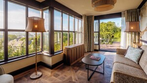 Un salon spacieux avec de grandes fenêtres, un plancher en bois et une vue sur la verdure et les bâtiments.