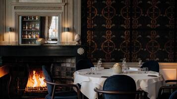 A warmly lit dining area with a fireplace, a bar with bottles, and patterned wallpaper.