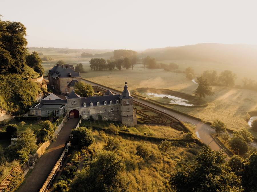 A castle with a moat, surrounded by lush greenery and a winding road.