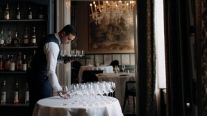Un serveur prépare les verres à vin sur une table dans un restaurant, avec une étagère à vin en arrière-plan.