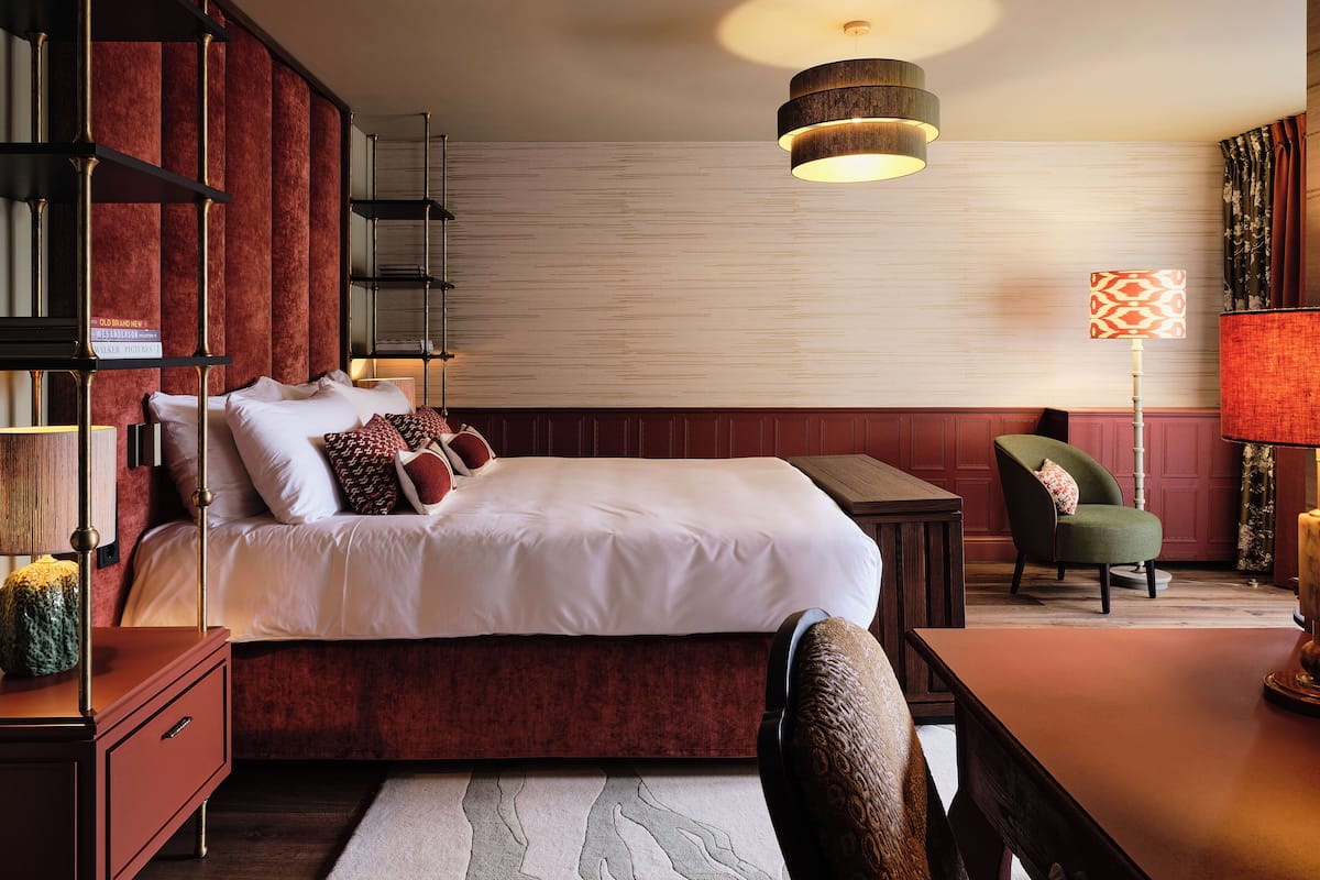 A bedroom with a large bed, a side table, a chair, a bookshelf, and a floor lamp.