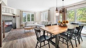 Una sala moderna con chimenea, un sofá grande, una mesa de comedor con sillas y vistas al exterior a través de amplios ventanales.