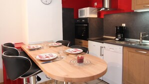 A modern kitchen with a wooden dining table, black chairs, a microwave, oven, dishwasher, and a coffee maker. - Cozy Studio for 4 with Balcony, Near Ski Lifts & Village Center (Les Gets)