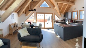 A spacious loft with a high ceiling, wooden beams, a dining area with a table and chairs, a kitchen with a sink and cabinets, and a cozy seating area with a sofa and a coffee table. - 4* Chalet for 8, sunny with wifi and pets allowed (Valloire)