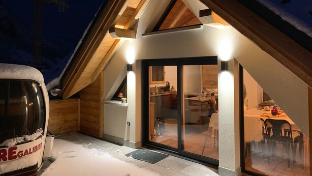 A modern, snow-covered building with a sloped roof, wooden beams, and a glass door entrance. - 4* Chalet for 8, sunny with wifi and pets allowed (Valloire)