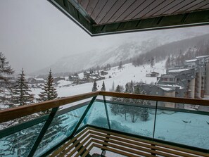 A snowy mountain village with a ski slope, viewed from a balcony with a glass railing.