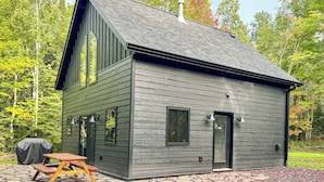A modern cabin with a steep gable roof, large windows, and a covered patio area. - Hodag House | Magical Cabin & Creature Comforts (Herbster)