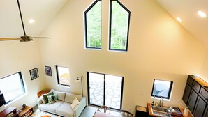 A spacious living area with a high ceiling, large windows, a sofa, a dining table, and a kitchen area. - Hodag House | Magical Cabin & Creature Comforts (Herbster)