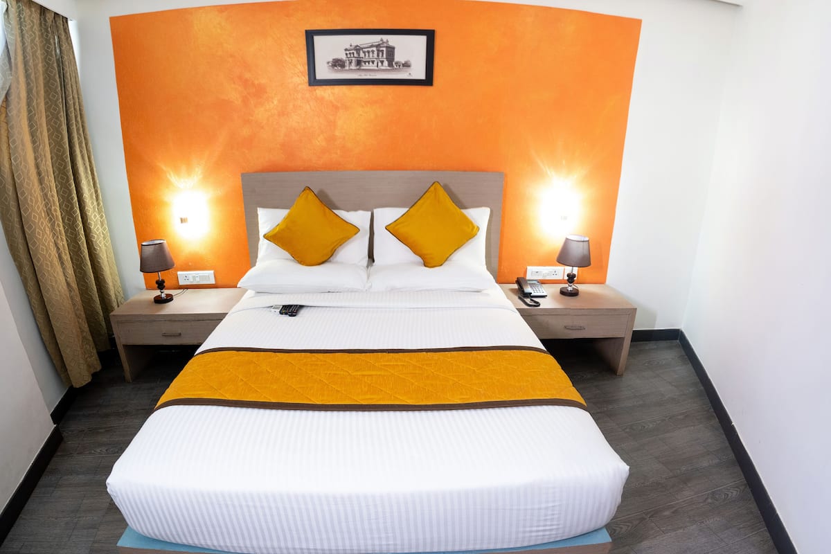 A hotel room with a large bed, two bedside tables, a ceiling fan, and an orange accent wall.