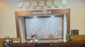 A reception desk with a marble wall backdrop, multiple clocks, and a sign reading "RECEPTION". - Hotel The Blackstone (Bengaluru)