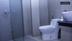 A modern bathroom with a glass shower enclosure, a white toilet, and a sink with a black countertop. - Hotel The Blackstone (Bengaluru)