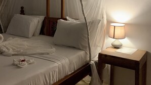A bed with a canopy, a bedside lamp, and a wooden nightstand. - Chokoro House (Paje)