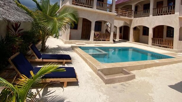 A resort with a swimming pool, lounge chairs, and palm trees. - Chokoro House (Paje)