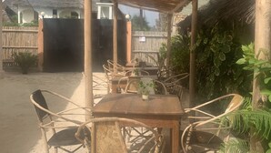 A covered outdoor seating area with a wooden table and wicker chairs, surrounded by a bamboo fence and thatched-roof structures. - Chokoro House (Paje)