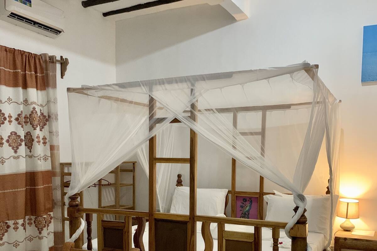 A wooden four-poster bed with a canopy, a wooden chair, a table, and a patterned rug.