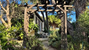 A wooden pergola structure in a garden with a pathway leading to a building. - Petite Maison Avec 2 Chambres 3 Personnes Avec Terrasse Propriété Fermée (Calvi)