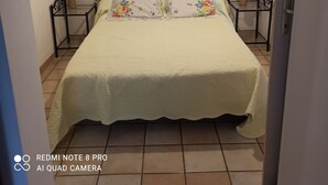 A bedroom with a bed, two bedside tables, and a door. - Petite Maison Avec 2 Chambres 3 Personnes Avec Terrasse Propriété Fermée (Calvi)
