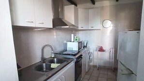 A compact kitchen with white cabinets, a stainless steel sink, a washing machine, and a refrigerator. - Petite Maison Avec 2 Chambres 3 Personnes Avec Terrasse Propriété Fermée (Calvi)