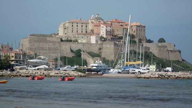 A historic fortified building with multiple levels and a prominent dome, surrounded by a marina with various boats. - Petite Maison Avec 2 Chambres 3 Personnes Avec Terrasse Propriété Fermée (Calvi)