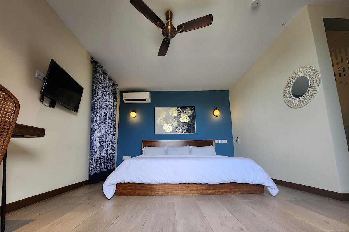 A bedroom with a bed, a ceiling fan, a wall-mounted TV, and an air conditioning unit.