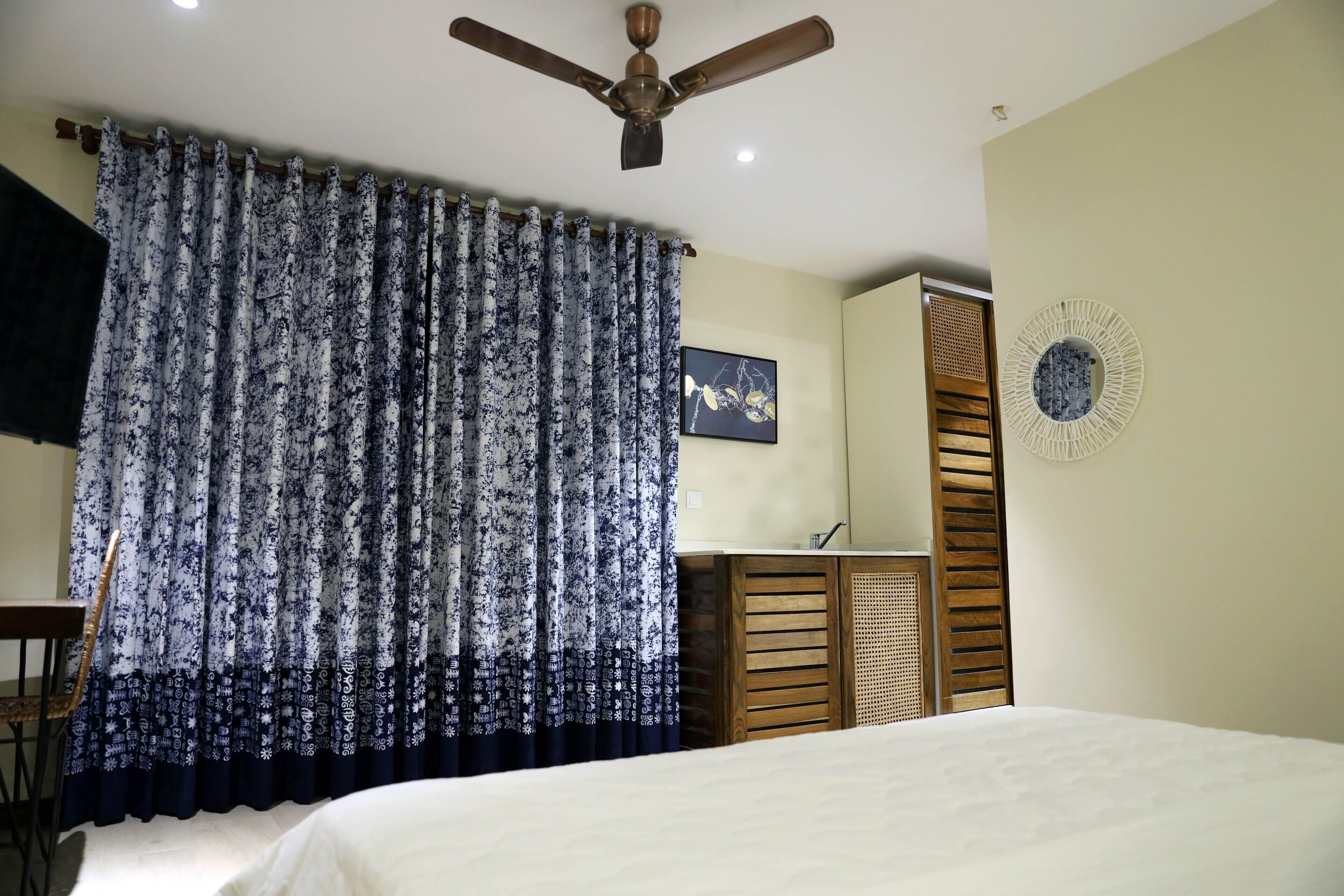 A bedroom with a bed, a ceiling fan, a curtain, a wall-mounted picture, and a wooden cabinet.