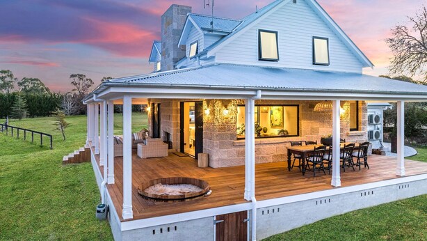 Une maison à deux étages dotée d’un patio couvert, d’une cheminée en pierre, d’un espace salon extérieur et d’un jacuzzi.