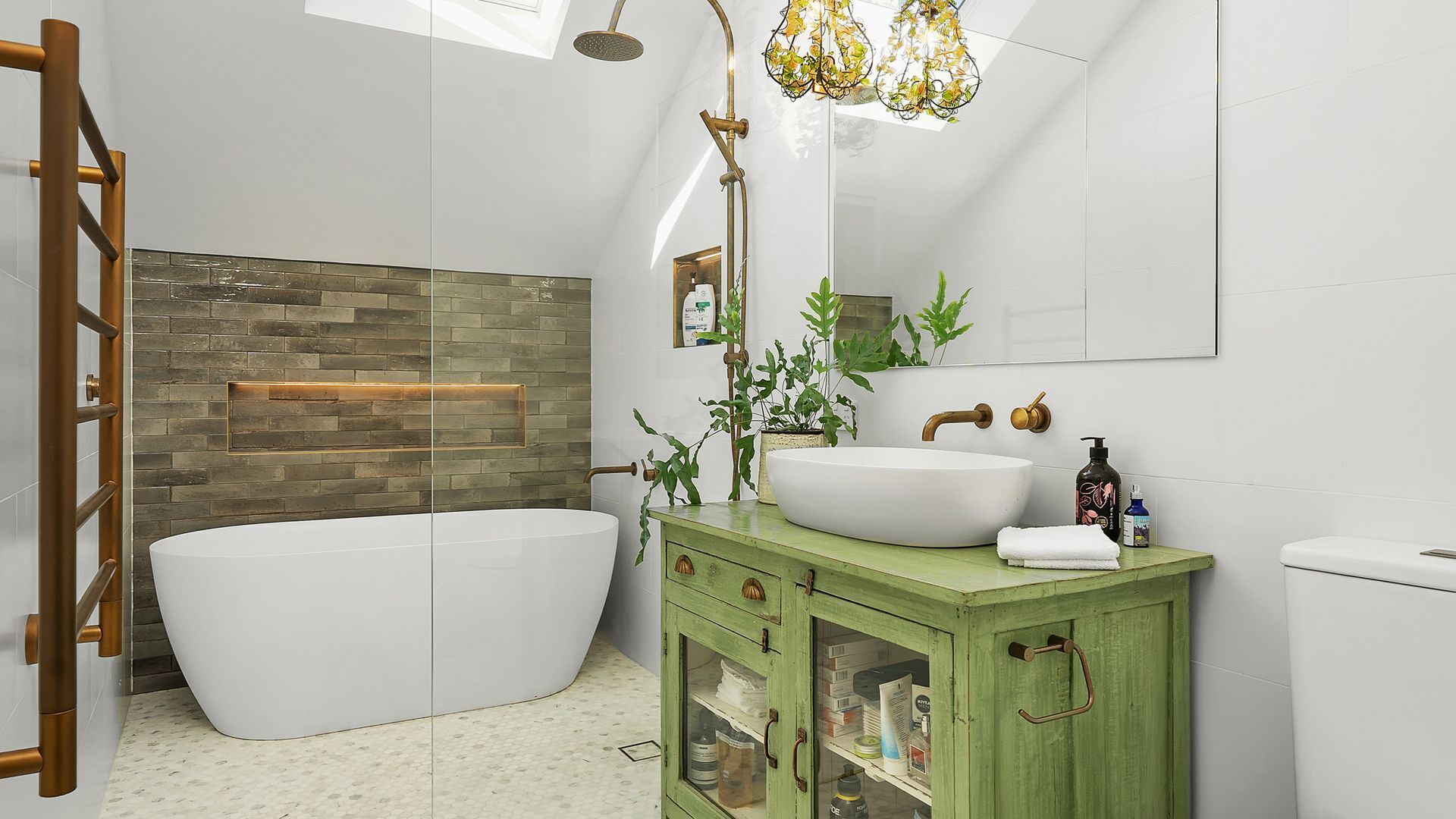 A modern bathroom with a freestanding bathtub, a green vanity with a large mirror, and a shower with a unique chandelier.
