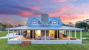 Une maison à deux étages dotée d’un porche abrité, d’une cheminée en pierre et offrant une vue sur le paysage environnant.