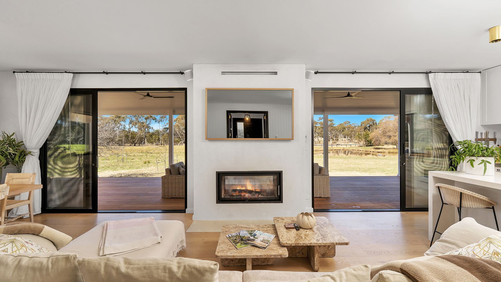 A modern living room with a fireplace, a sofa, a coffee table, and a dining area with a view of the outdoors.