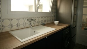 A kitchen with a large white sink, a stainless steel refrigerator, and a window above the sink. - Charming House Near Beach and Shops with Private Parking and Terrace (La Tranche-sur-Mer)