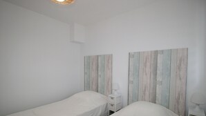 A room with two single beds, white bedding, and a white nightstand with a lamp. - Charming House Near Beach and Shops with Private Parking and Terrace (La Tranche-sur-Mer)