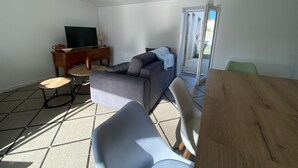 A living room with a sofa, a television, a wooden table, and a chair. - Charming House Near Beach and Shops with Private Parking and Terrace (La Tranche-sur-Mer)