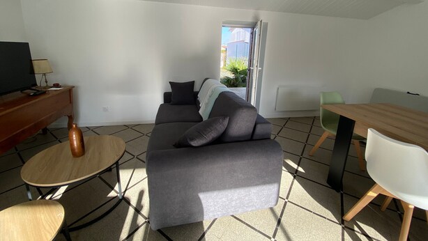 A modern living room with a grey sofa, a wooden coffee table, a TV, and a dining table with chairs. - Charming House Near Beach and Shops with Private Parking and Terrace (La Tranche-sur-Mer)