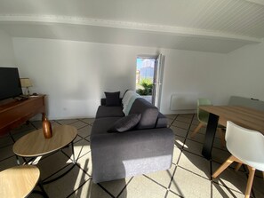 A modern living room with a grey sofa, a wooden coffee table, a TV, and a dining table with chairs. - Charming House Near Beach and Shops with Private Parking and Terrace (La Tranche-sur-Mer)