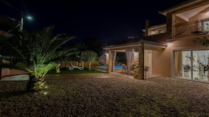 A modern house with a pool, stone pillars, and a covered patio area.