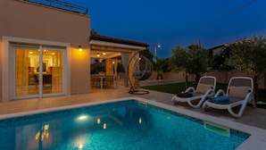 A swimming pool with lounge chairs, a hanging chair, and a patio area with a table and chairs.