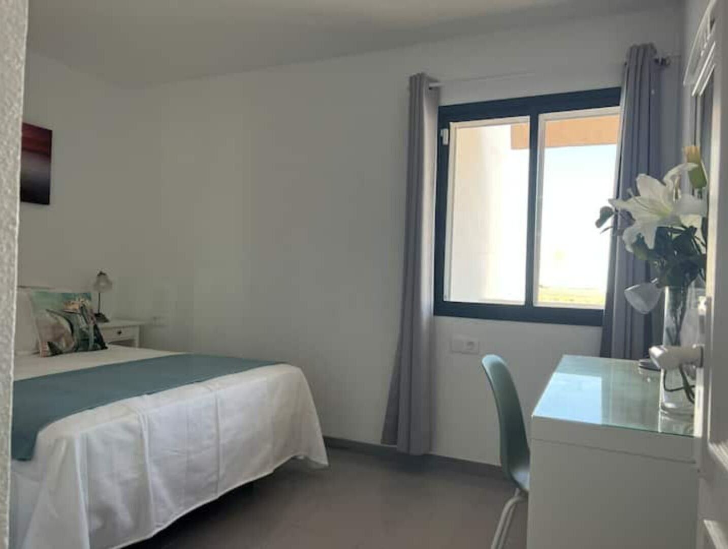 Quarto de hotel com cama, escrivaninha e janela com cortinas.