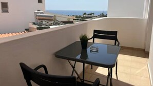 A balcony with a table and chairs, a potted plant, and a view of the sea.