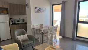 A modern apartment with a dining area, kitchen, and a balcony with curtains.